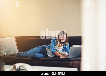 La vie est tellement plus facile quand vous vous détendez. une jeune femme détendue utilisant un ordinateur portable sur le canapé à la maison. Banque D'Images