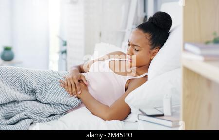 C'est insupportable. une jeune femme attirante souffrant de crampes d'estomac tout en étant allongé dans son lit à la maison. Banque D'Images