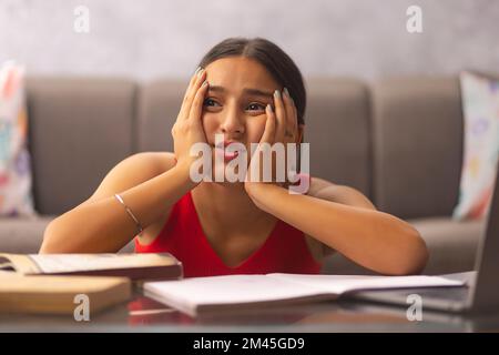 Portrait d'une adolescente fatiguée regardant loin avec les mains sur les joues pendant la classe en ligne Banque D'Images