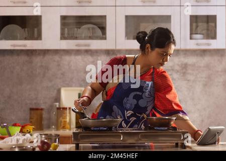 Femme suivant la recette sur un comprimé tout en cuisinant dans la cuisine Banque D'Images