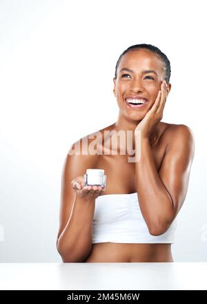 Ce produit fonctionne prodiges filles. Studio portrait d'une belle jeune femme appliquant un hydratant de peau sur son visage tout en se tenant à côté d'un blanc Banque D'Images