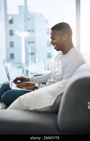 D'accord Je suis coupable Je ne suis pas au bureau. un beau jeune homme assis sur un canapé et utilisant son ordinateur portable à la maison. Banque D'Images