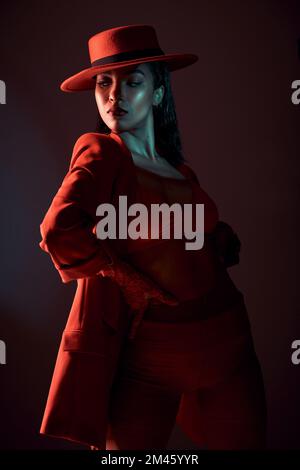 Mode, rouge et branché avec une femme noire modèle en studio sur un fond sombre pour un style tendance ou contemporain. Créatif, chapeau et vêtements avec un Banque D'Images
