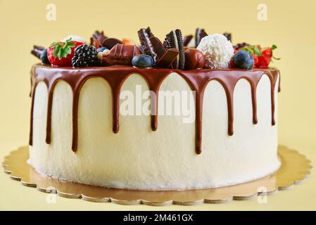 Gâteau d'anniversaire sur fond jaune. Gros plan de gâteau décoré de baies fraîches et de bonbons au chocolat sur fond de couleur. Délicieux dessert pour la fête Banque D'Images