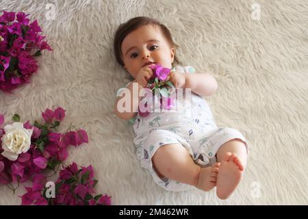 Joli jeu de bébé avec bougainvilliers fleur et sourire sur blanc couverture moelleuse. Banque D'Images