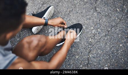 Le laçage pour la route qui vous précède. Photo en grand angle d'un sportif qui noue ses lacets tout en faisant de l'exercice à l'extérieur. Banque D'Images