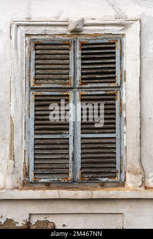 Vieille fenêtre avec des volets en bois usés sur le mur extérieur d'une ancienne maison en ruines Banque D'Images