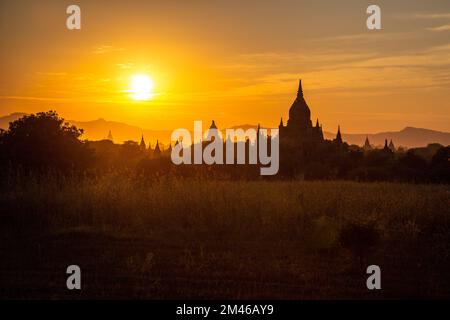 Les clochers de certains des nombreux temples de Bagan sont silhouettés par le soleil couchant du Myanmar. Banque D'Images