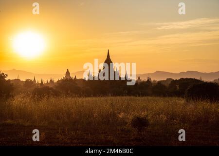 Les clochers de certains des nombreux temples de Bagan sont silhouettés par le soleil couchant du Myanmar. Banque D'Images