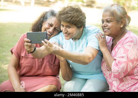 Des femmes indiennes heureuses utilisant un smartphone et prenant des photos d'elles-mêmes en plein air dans le parc d'été. Personnes âgées en cliquant sur selife . Banque D'Images