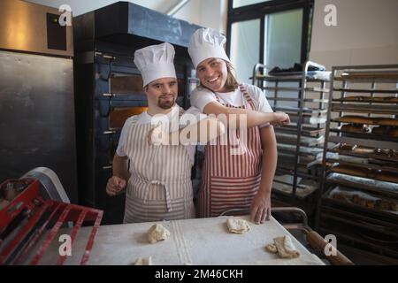 Portrait de l'homme avec le syndrom bas et son collègue dans la boulangerie. Concept d'intégration les personnes handicapées dans la société. Banque D'Images