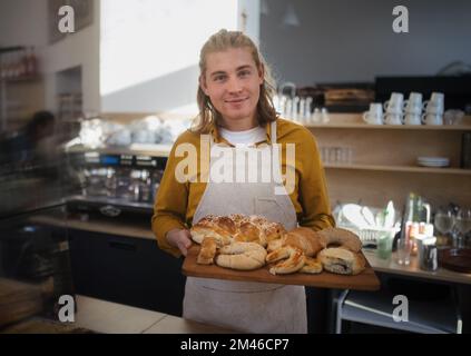 Jeune homme travaillant dans un café, carring des pâtisseries fraîches. Banque D'Images