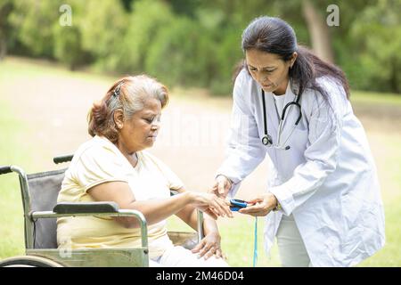 Un médecin indien vérifie avec un dispositif d'oxymètre de pouls sur le doigt d'une patiente âgée atteinte du diabète dans un fauteuil roulant à l'extérieur du parc. Banque D'Images