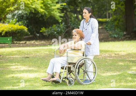 Infirmière indienne soignant prenant soin de la patiente senior en fauteuil roulant à l'extérieur du parc, un médecin asiatique aide et soutient les personnes âgées âgées âgées Banque D'Images