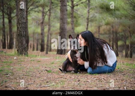Une jeune femme caucasienne embrasse son chien mixte dans une forêt de pins. Banque D'Images