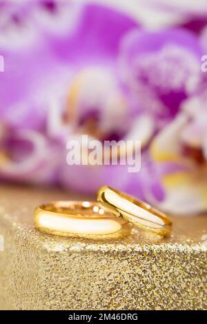 Anneaux dorés de mariage sur un piédestal doré derrière des orchidées violettes. Verticale Banque D'Images