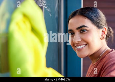 Femme, nettoyage et lavage de fenêtre avec un sourire pour nettoyer les fenêtres de saleté avec de l'eau, du savon et du tissu. Bonne femme de ménage indienne ou femme de ménage qui fait le printemps Banque D'Images