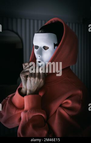 Portrait de la femme en masque blanc et capuche sur fond noir. Notion de troubles mentaux, hypocrisie. Photo de haute qualité Banque D'Images