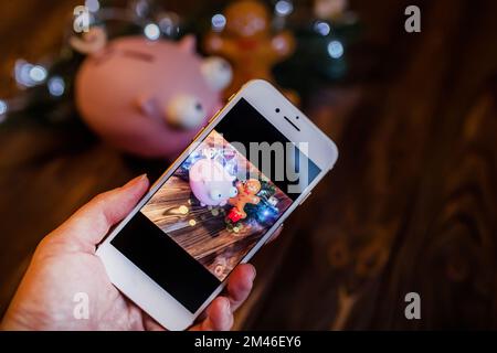 Tournage au téléphone les affaires de Noël encore la vie avec une banque de piggy et une guirlande avec lanternes. Main tenant un smartphone. Apprendre à prendre des photos Banque D'Images