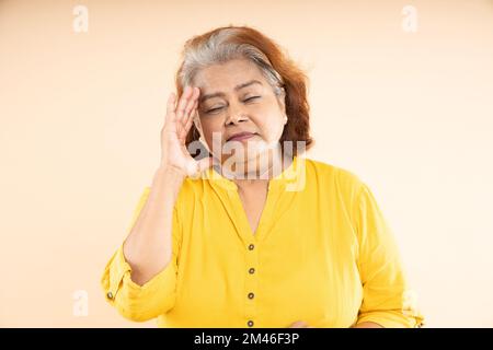 Femme indienne âgée souffrant de maux de tête debout à l'extérieur du parc. Personnes âgées stressées et souffrant d'hypertension. Banque D'Images