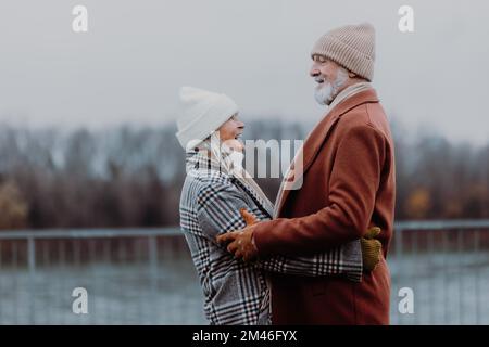 Élégant couple senior marchant près de la rivière, pendant la journée froide d'hiver. Banque D'Images