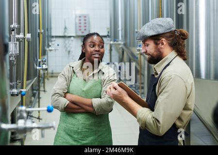 Un travailleur de la brasserie parle au directeur lorsqu'il se trouve parmi les réservoirs avec des boissons fermenantes Banque D'Images