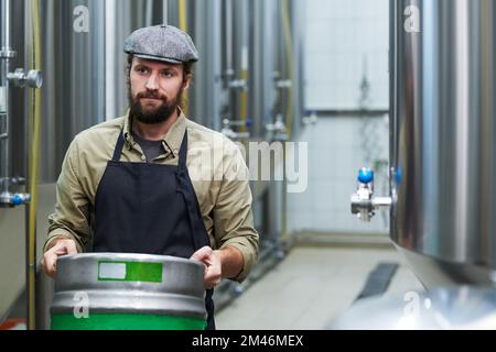 Propriétaire de microbrasserie barbu transportant le fût avec la bière à l'entrepôt Banque D'Images