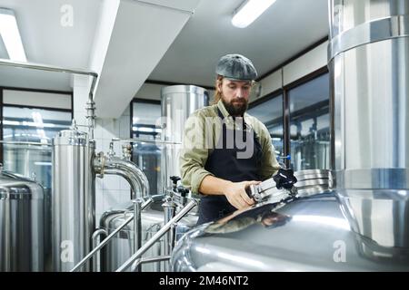 Un petit ouvrier de brasserie vérifie les réservoirs avec de la bière fermentée Banque D'Images