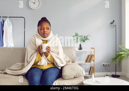 Une jeune femme afro-américaine malade se sent mal et boit une boisson chaude. Banque D'Images