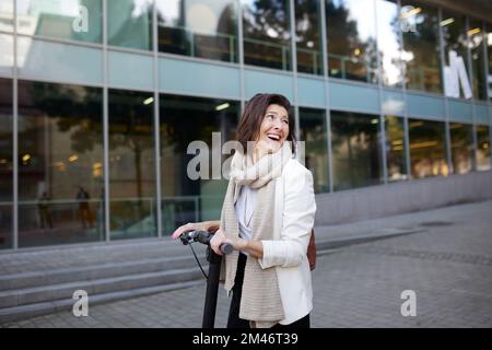 Femme d'affaires souriante utilisant un scooter électrique Banque D'Images