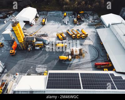 Vue aérienne des terrains de la société de construction, des panneaux solaires sur le toit et des camions jaunes stationnés sur le site Banque D'Images