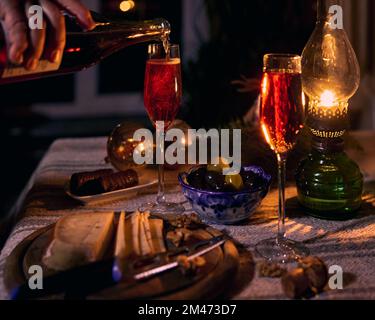 Une main versant du vin mousseux rose dans un verre, deux verres avec du vin, des olives dans un bol en céramique bleue. Composition de la table de Noël. Banque D'Images