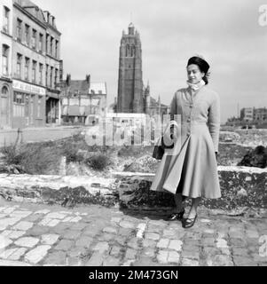 Femme française portant des vêtements de style 1940s ou de mode y compris le manteau plissé serré Dunkerque France 1949. En arrière-plan se trouve le beffroi sur pied avec un premier plan ruiné ou vacant, à la suite de dommages de guerre ou de bombardements pendant la Seconde Guerre mondiale, avant la reconstruction de Dunkerque après la guerre. Banque D'Images