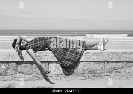 Jeune française ou 1950s femme portant un Tartan, un motif à carreaux, une robe à carreaux ou à carreaux recrée ou se détend sur le Seawall à Hendaye Pyrénées-Atlantiques France 1950 Banque D'Images