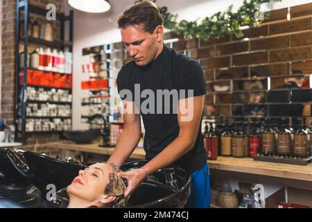 Jeune femme heureuse et détendue ayant un salon de coiffure et un massage de la tête fait par un coiffeur professionnel de sexe masculin. Intérieur du salon de coiffure. Photo de haute qualité Banque D'Images