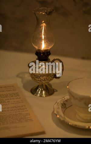 photo d'une lampe au kérosène, d'un vieux livre ouvert, d'une tasse vide et d'une soucoupe sur la table Banque D'Images