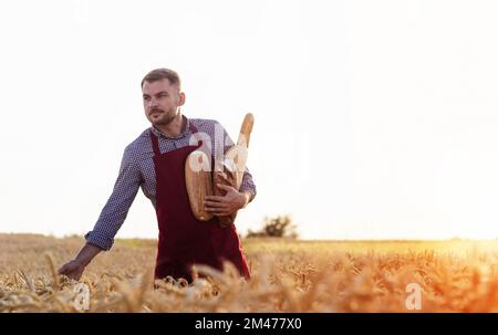 Farmworker tenant des pains dans ses mains tout en marchant dans le champ de blé. Banque D'Images