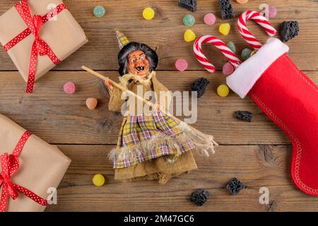 La sorcière Befana et le stockage rouge avec du charbon doux et des bonbons sur fond de bois rustique. Tradition italienne d'Epiphanie Banque D'Images