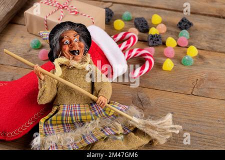 La sorcière Befana et le stockage rouge avec du charbon doux et des bonbons sur fond de bois rustique. Tradition italienne d'Epiphanie Banque D'Images