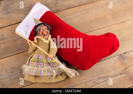 La sorcière drôle Befana et le stockage rouge avec du charbon doux et des bonbons sur fond de bois. Tradition italienne d'Epiphanie Banque D'Images