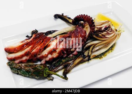 tentacule d'octopus de style méditerranéen grillé au feu de bois avec des quartiers de padron, de chicorée et de citron Banque D'Images