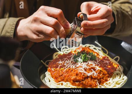 Vous pouvez râper les mains de délicieux parmesan sur des pâtes italiennes bolognaises fraîchement préparées. Petite boîte de râpe à fromage. Cuisine italienne, recette de pâtes bolognaises Banque D'Images