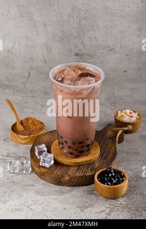 Boba ou perles de tapioca est le thé de lait à bulles de taïwan dans une tasse en plastique avec saveur de chocolat noir sur fond de texture, rafraîchissement d'été. Banque D'Images