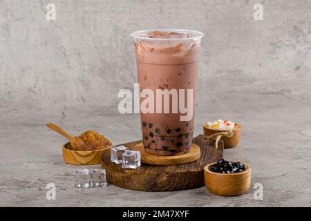 Boba ou perles de tapioca est le thé de lait à bulles de taïwan dans une tasse en plastique avec saveur de chocolat noir sur fond de texture, rafraîchissement d'été. Banque D'Images