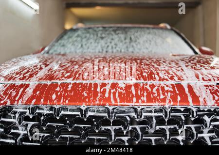 Voiture sport rouge moderne de luxe recouverte de mousse. Lavage de voiture. Photo en gros plan du capot de voiture dans le service de lavage de voiture intérieur. Banque D'Images