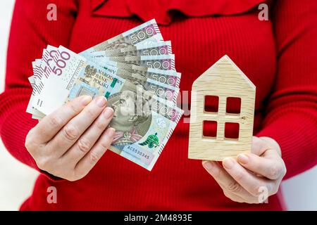Le concept du coût de possession d'un appartement en Pologne, D'Une maison en bois tenue dans la main et d'un paquet de 500 billets de banque zloty, le concept de haut hou Banque D'Images