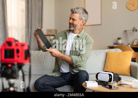 Travail moderne et passe-temps. Sourire mature caucasien homme blogueur de tournage vidéo blog, regardant la tablette Banque D'Images