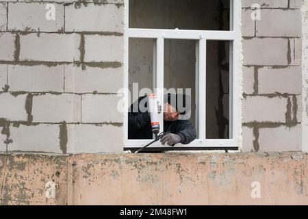 Tiraspol, Moldova - 6 décembre 2022: Le travailleur applique de la mousse de polyuréthane pour combler l'espace entre la ceinture et le cadre de la fenêtre. Créer le confort et le confort pour Banque D'Images