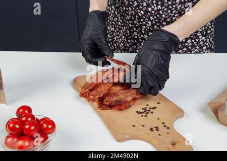 un gars met de la viande séchée dans des boîtes en papier dans des gants noirs. Photo de haute qualité Banque D'Images