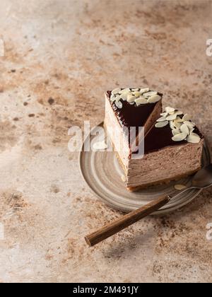 Deux tranches de cheesecake au chocolat avec pétales d'amande sur plaque en céramique sur fond texturé brun. Composition minimale. Espace texte, menu. Vertical o Banque D'Images